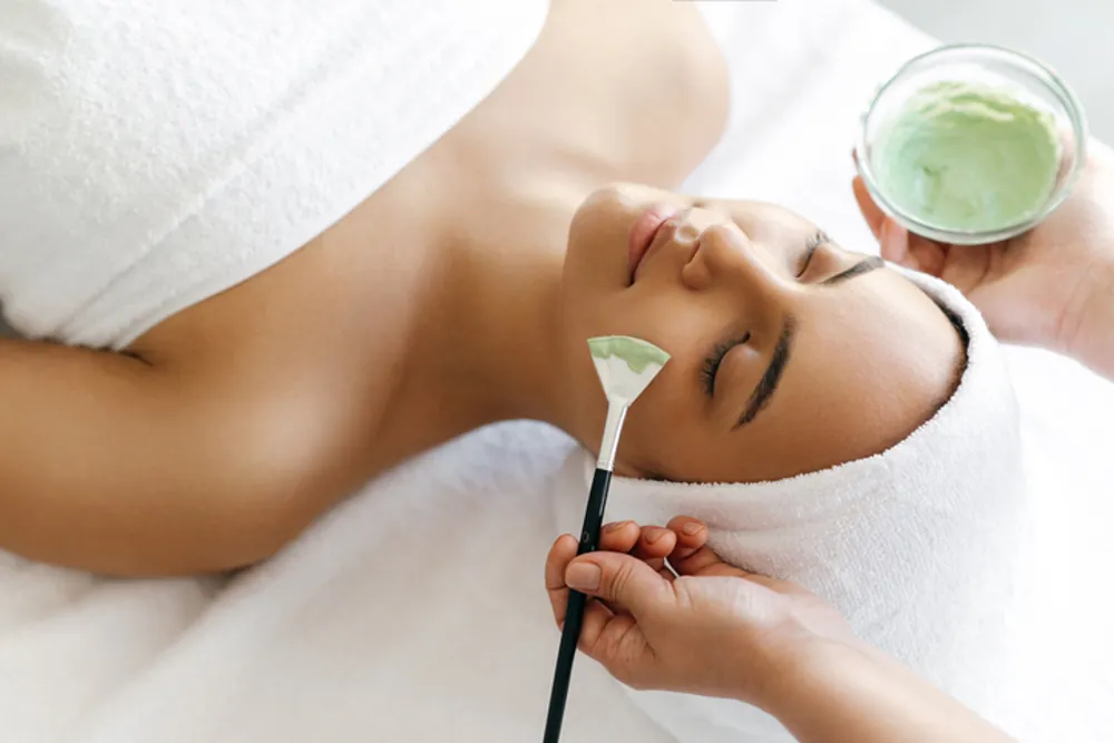 Esthetician applying a green clay facial mask during a facial at Uplift Wellness & Aesthetics in Monteagle, TN